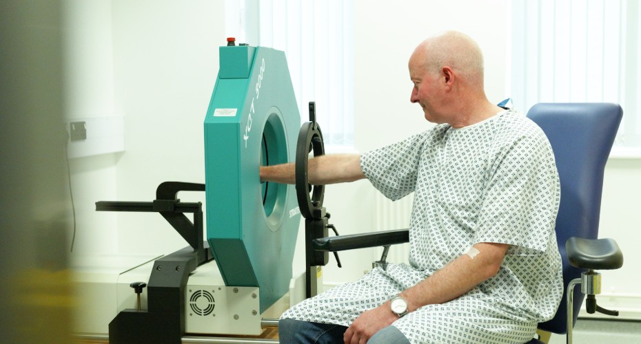 A man seated in a chair next to a pqct machine, engaged in a medical examination.