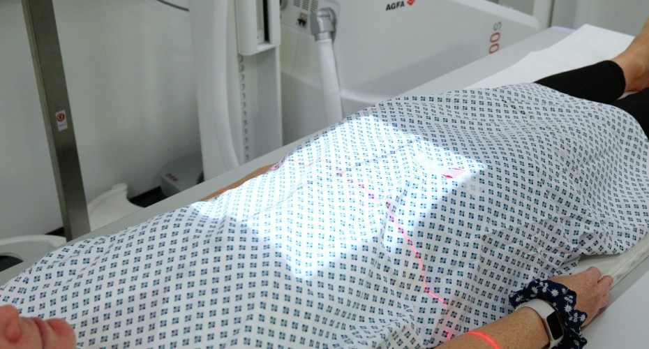 A woman lying on a bed, illuminated by light, undergoing a patient abdominal x-ray examination.